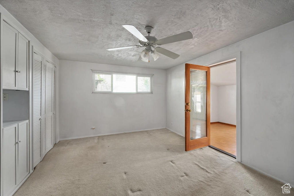 Unfurnished bedroom with light colored carpet, ceiling fan, a textured ceiling, baseboards, and a closet