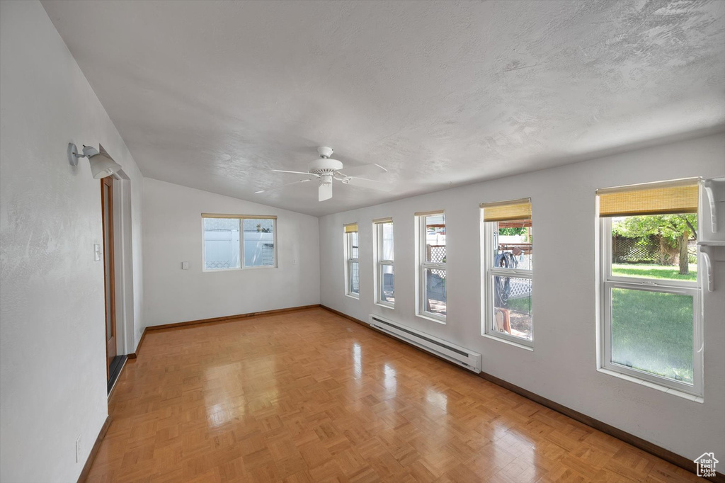Unfurnished room with baseboard heating, baseboards, vaulted ceiling, plenty of natural light, and ceiling fan