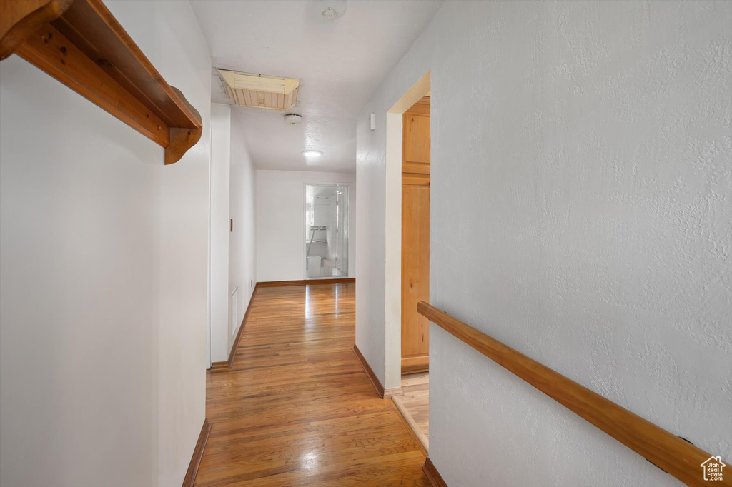 Hallway with light wood finished floors, baseboards, and an upstairs landing