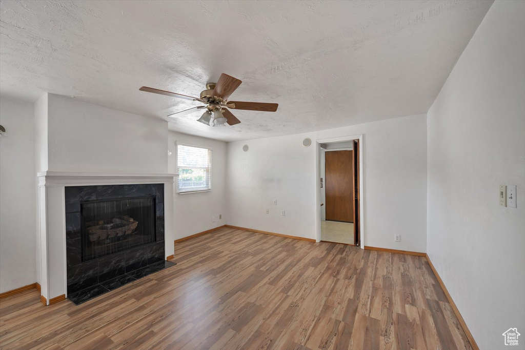 Unfurnished living room featuring wood finished floors, a premium fireplace, baseboards, and a textured ceiling