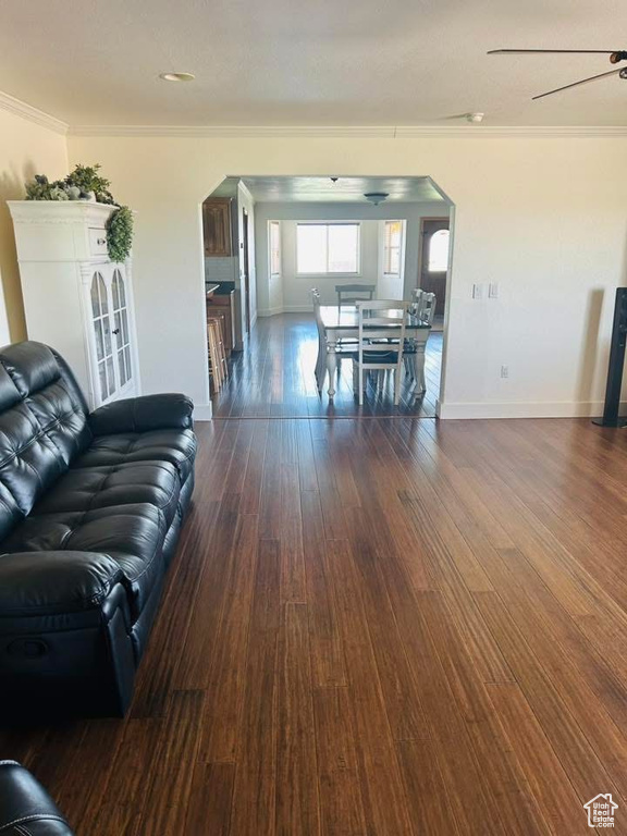 Living area with crown molding, arched walkways, baseboards, and dark wood finished floors