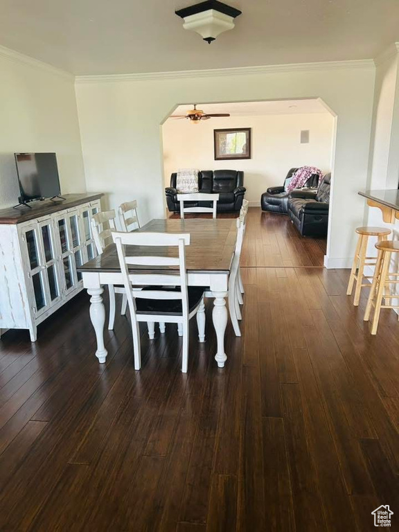 Dining space with arched walkways, ornamental molding, dark wood-style flooring, and a ceiling fan