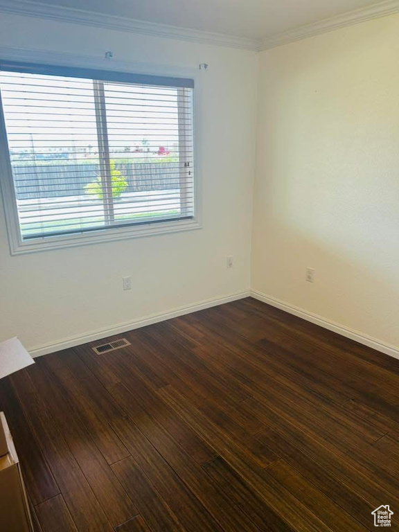 Empty room with dark wood-style floors, baseboards, and crown molding