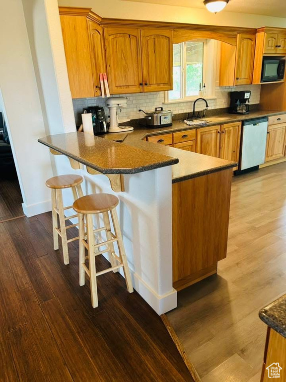 Kitchen featuring dishwasher, black microwave, a sink, dark wood-type flooring, and backsplash
