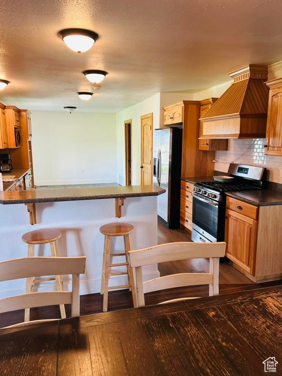 Kitchen featuring stainless steel appliances, a breakfast bar area, dark wood-style flooring, tasteful backsplash, and a textured ceiling