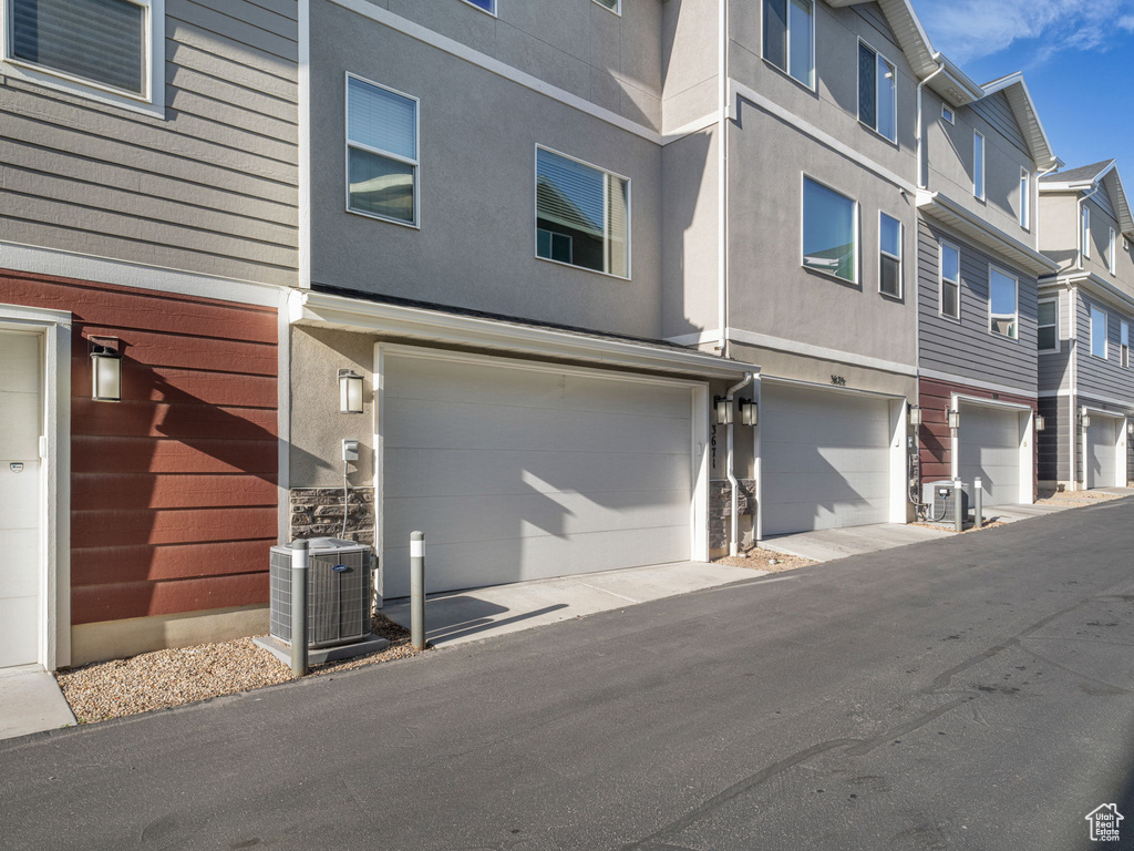 View of front of house with central AC, an attached garage, a residential view, stone siding, and stucco siding