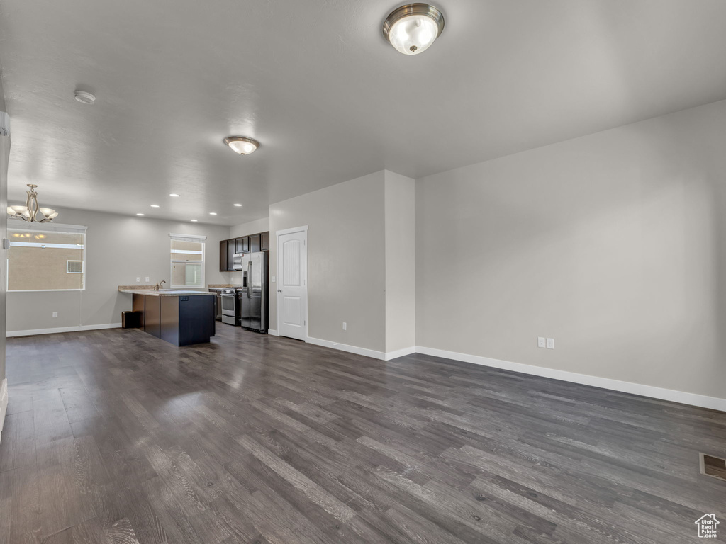 Unfurnished living room featuring a chandelier, dark wood-type flooring, baseboards, and recessed lighting