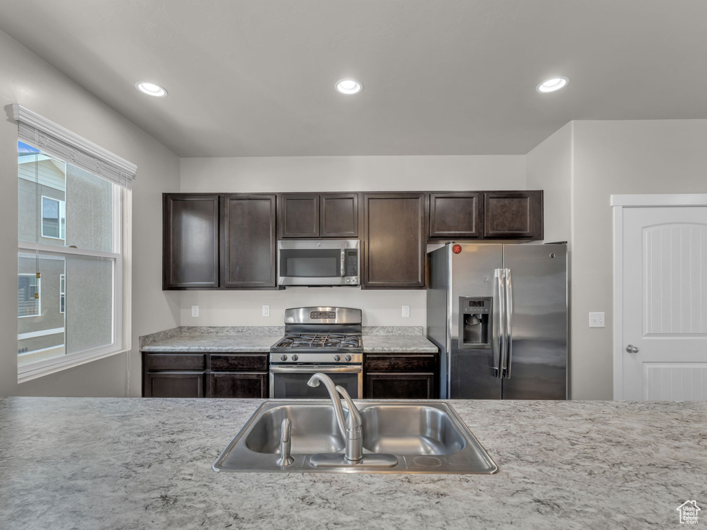 Kitchen with appliances with stainless steel finishes, a sink, dark brown cabinetry, light countertops, and recessed lighting