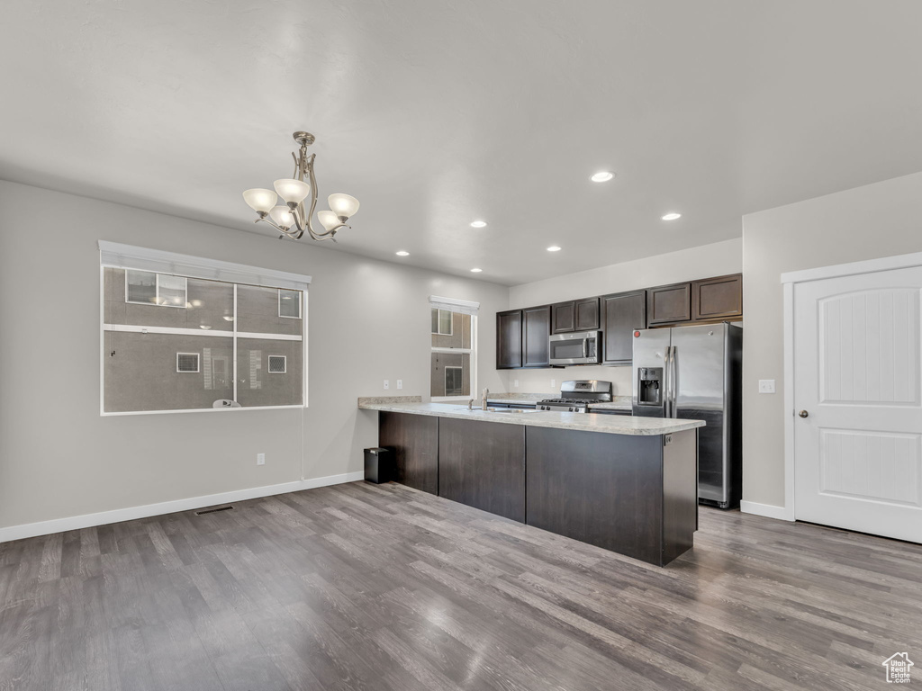 Kitchen featuring stainless steel appliances, a chandelier, a peninsula, dark brown cabinets, and baseboards