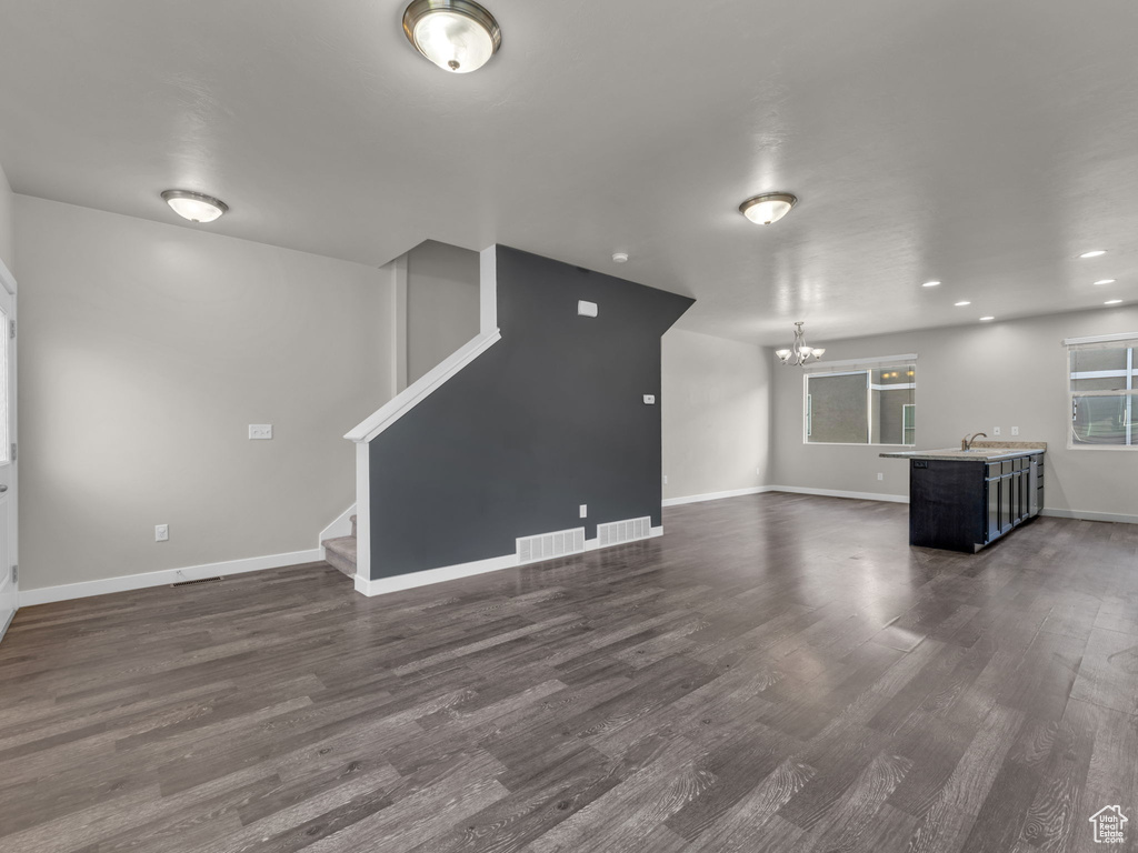 Unfurnished living room with a chandelier, dark wood-style flooring, baseboards, stairway, and recessed lighting