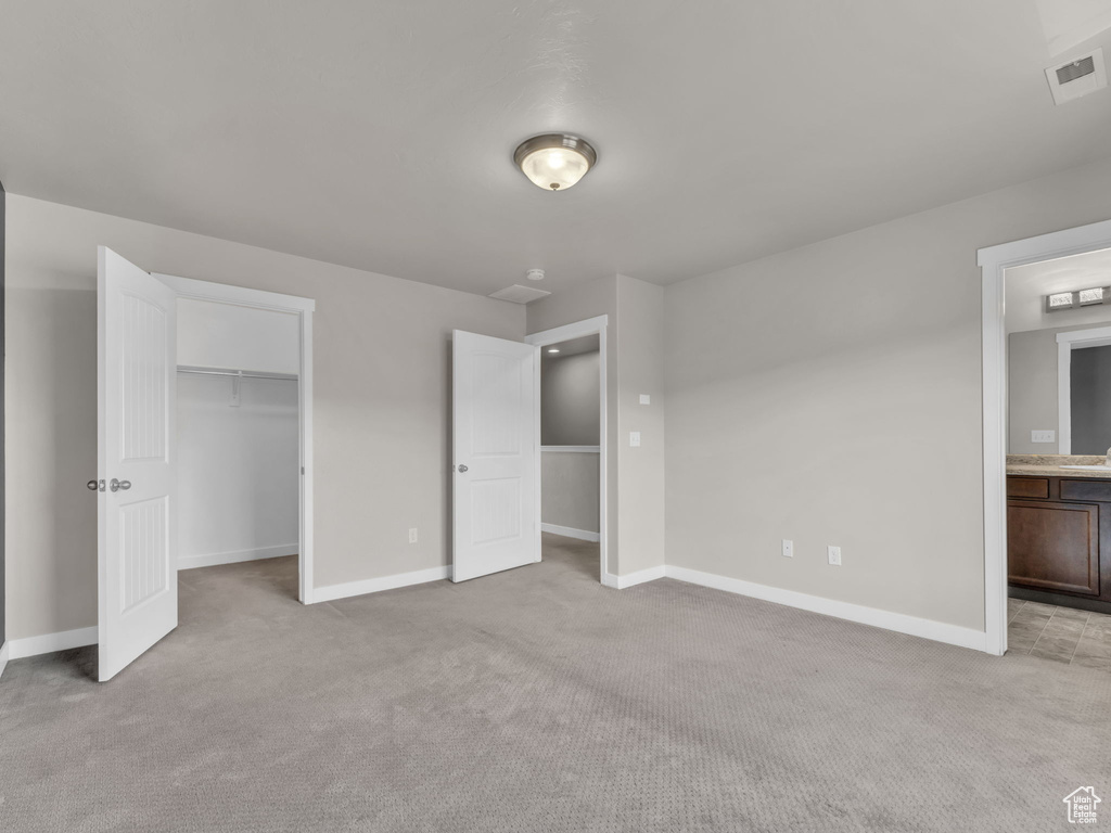 Unfurnished bedroom with light carpet, baseboards, a spacious closet, and ensuite bathroom