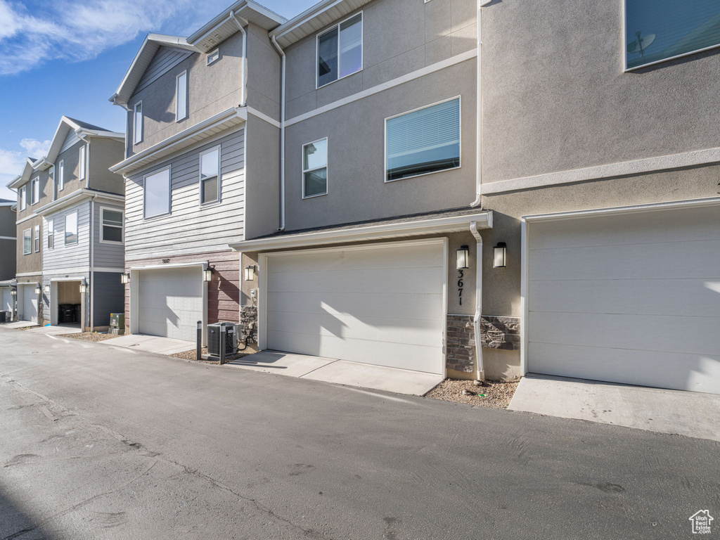 View of front of property with an attached garage, stone siding, central AC, and stucco siding