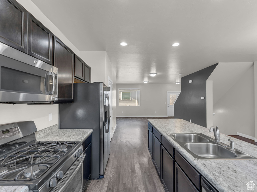 Kitchen with stainless steel appliances, a sink, wood finished floors, light countertops, and recessed lighting