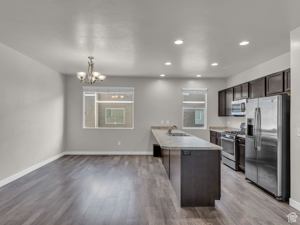 Kitchen with appliances with stainless steel finishes, dark brown cabinetry, a peninsula, a sink, and light countertops