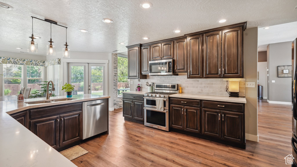 Kitchen with appliances with stainless steel finishes, a sink, light countertops, dark brown cabinetry, and backsplash