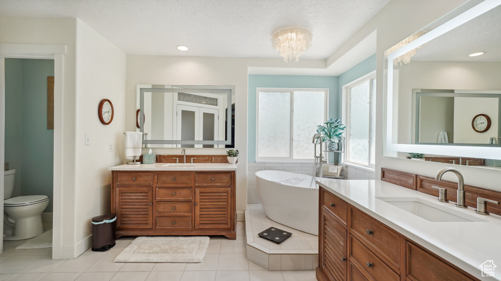 Bathroom with two vanities, a freestanding tub, tile patterned floors, toilet, and a chandelier