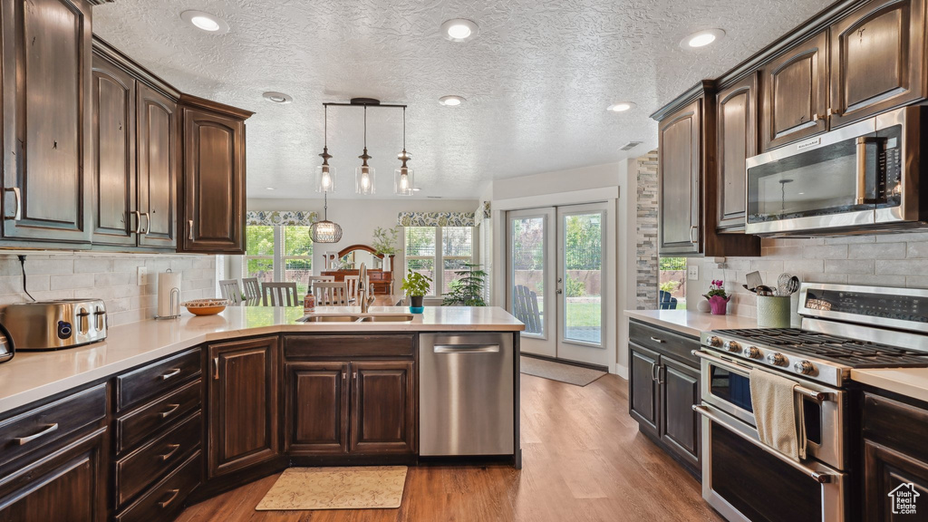 Kitchen with stainless steel appliances, light countertops, a sink, light wood finished floors, and a textured ceiling