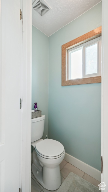 Bathroom with toilet, tile patterned flooring, baseboards, and a textured ceiling