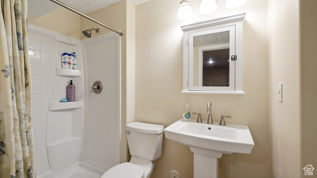 Bathroom with toilet, tiled shower, and a sink