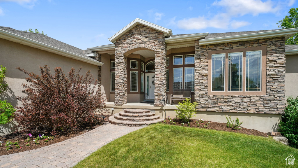 Property entrance with stone siding, a yard, covered porch, and stucco siding
