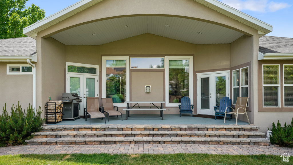 Doorway to property with french doors, stucco siding, a patio, and roof with shingles