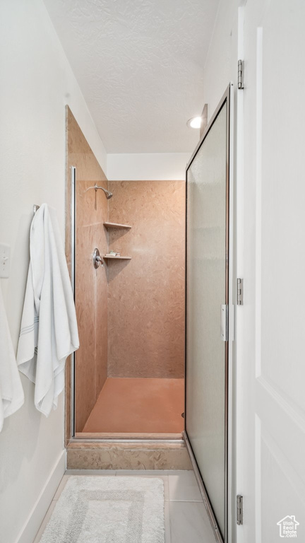 Full bathroom with a stall shower, tile patterned flooring, a textured ceiling, and baseboards