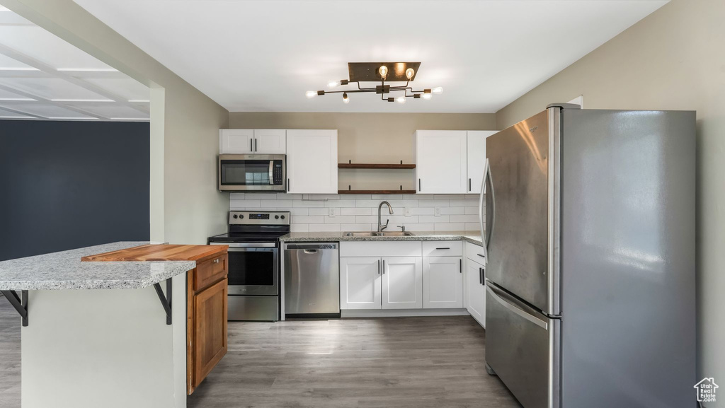 Kitchen with stainless steel appliances, open shelves, a sink, decorative backsplash, and light wood finished floors