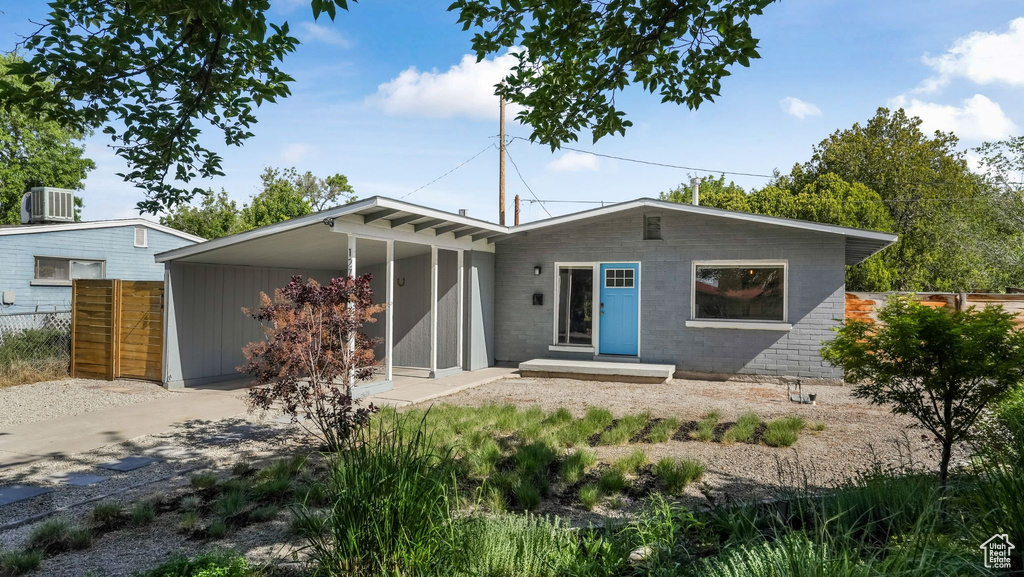 View of front of property featuring driveway, a carport, central AC, and concrete block siding