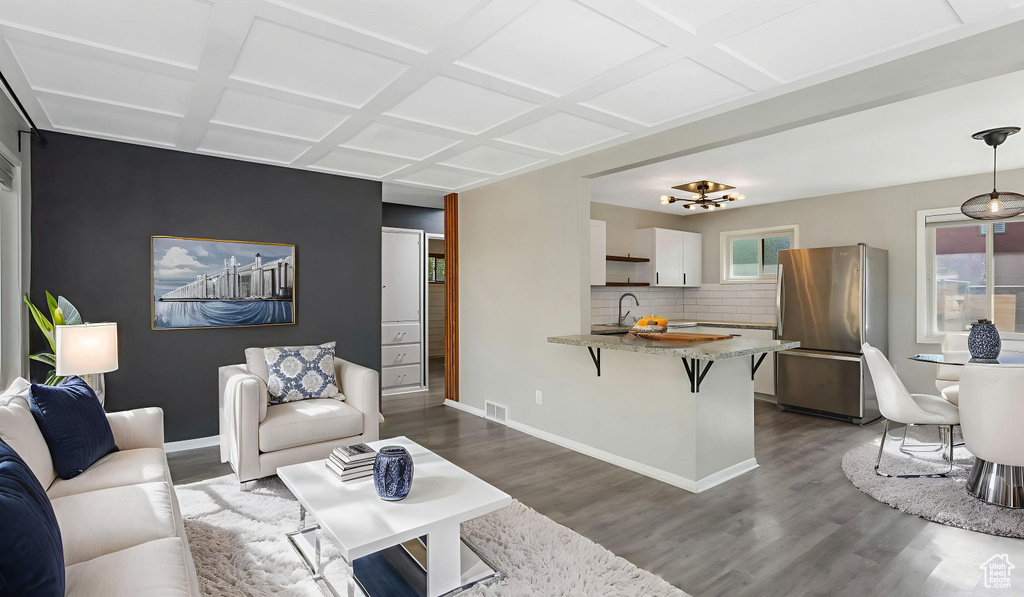 Living area with dark wood-style floors, coffered ceiling, baseboards, and a chandelier