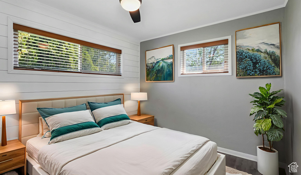 Bedroom with multiple windows, wood finished floors, crown molding, ceiling fan, and wooden walls