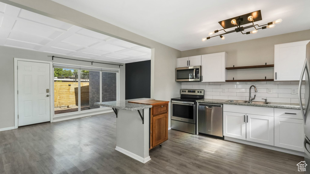 Kitchen featuring stainless steel appliances, a sink, open shelves, backsplash, and dark wood-style flooring