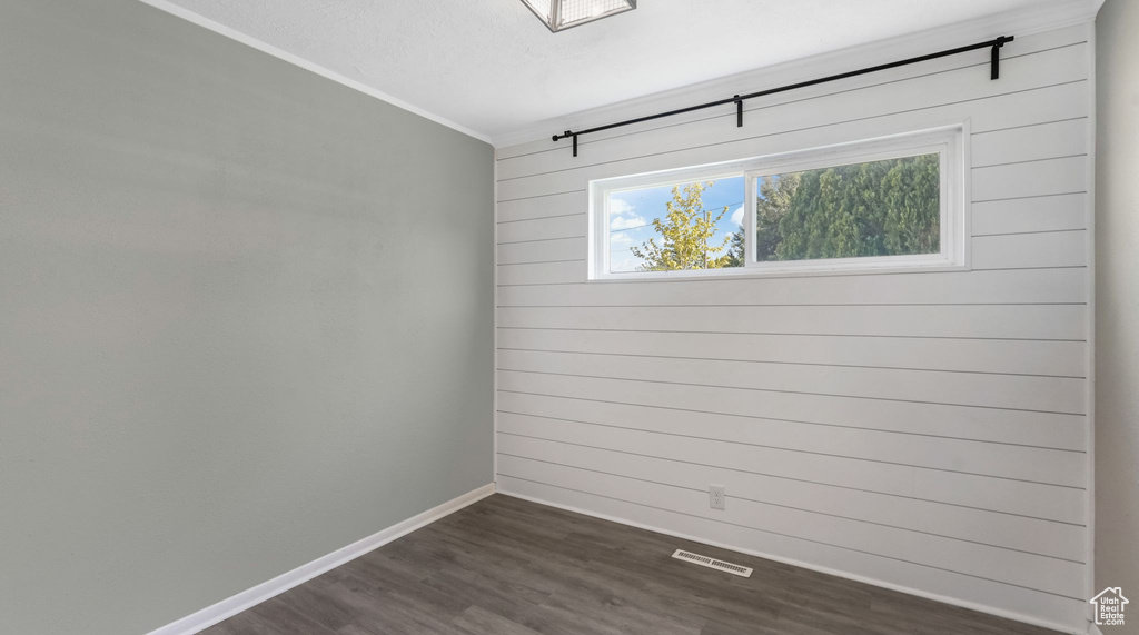 Spare room featuring dark wood-style flooring, baseboards, crown molding, and wooden walls