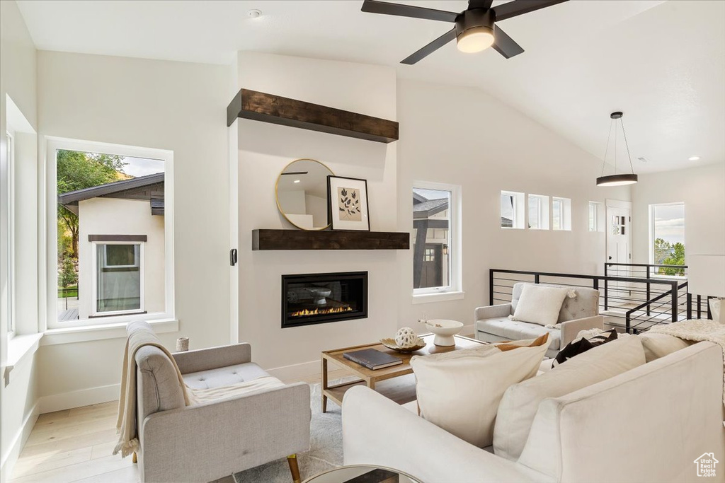 Living room featuring light wood-type flooring, a ceiling fan, vaulted ceiling, baseboards, and a glass covered fireplace