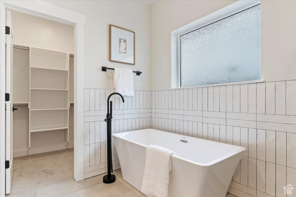 Bathroom with a freestanding bath, a wainscoted wall, a spacious closet, tile walls, and tile patterned flooring