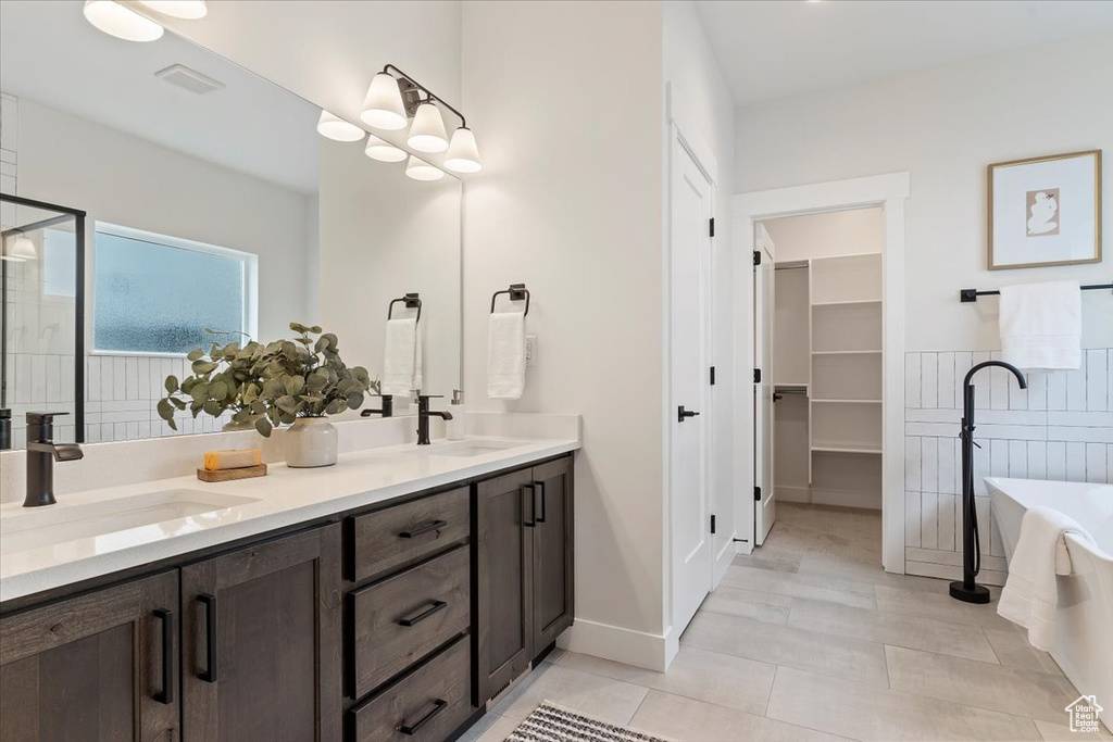 Full bath featuring double vanity, a freestanding bath, a stall shower, a spacious closet, and tile patterned flooring
