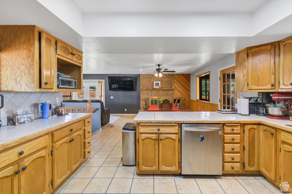 Kitchen featuring stainless steel dishwasher, ceiling fan, a peninsula, a fireplace, and light tile patterned floors