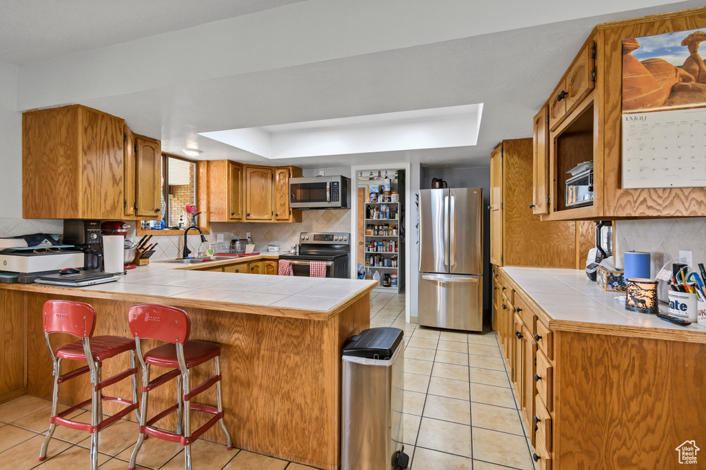 Kitchen with stainless steel appliances, a raised ceiling, a sink, a peninsula, and tasteful backsplash