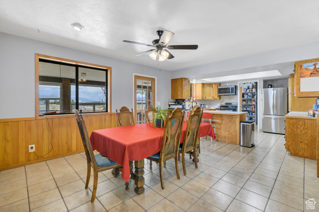 Dining area featuring wainscoting, a ceiling fan, wooden walls, and light tile patterned floors