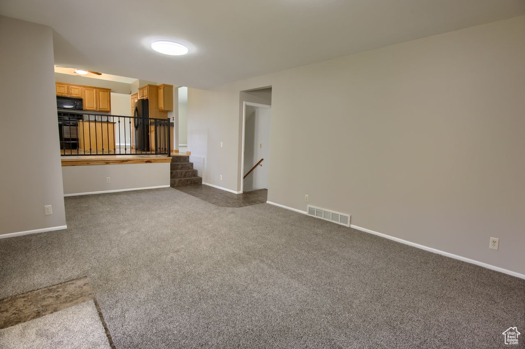 Unfurnished living room featuring dark colored carpet and baseboards