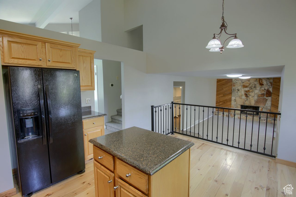 Kitchen featuring black fridge with ice dispenser, light wood-style floors, a chandelier, high vaulted ceiling, and a center island