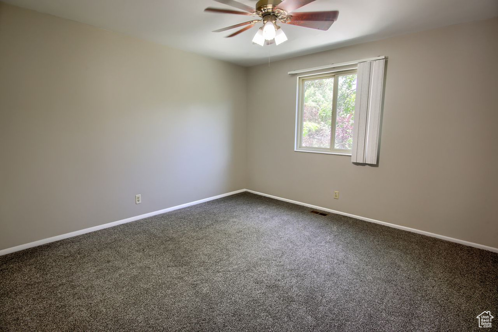 Spare room with dark carpet, a ceiling fan, and baseboards