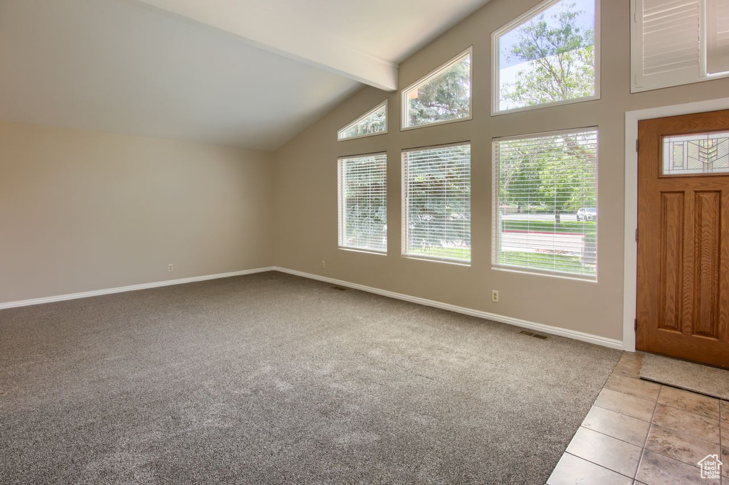 Carpeted entrance foyer featuring plenty of natural light, baseboards, beam ceiling, tile patterned floors, and high vaulted ceiling