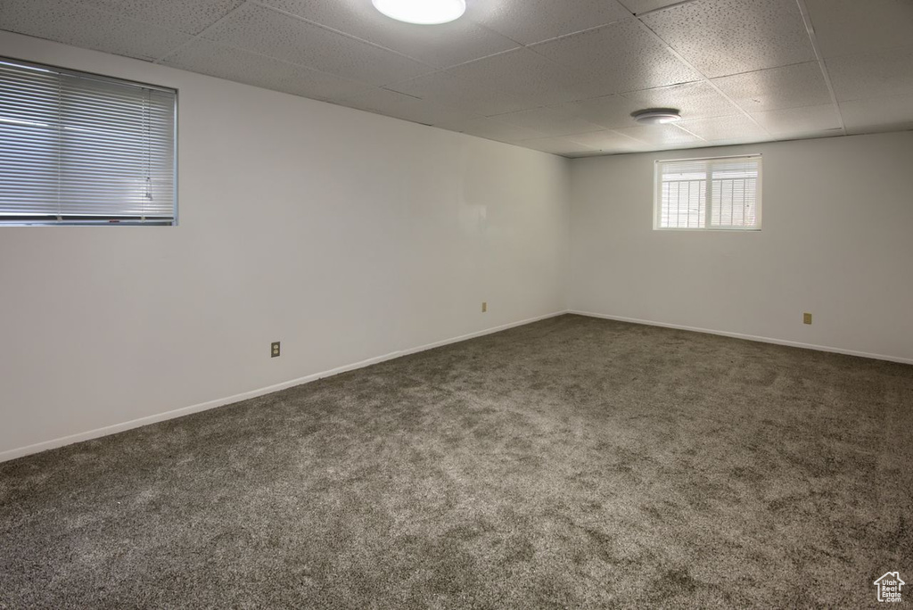 Unfurnished room with a paneled ceiling, dark colored carpet, and baseboards