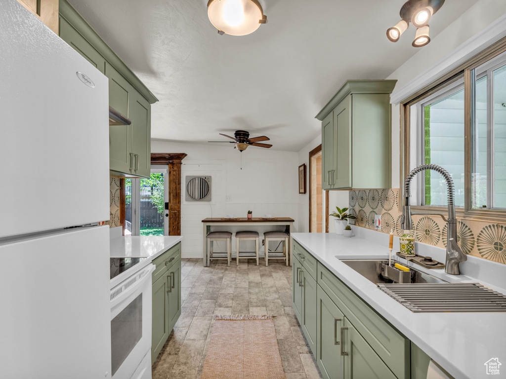 Kitchen with green cabinetry, white appliances, a sink, and light countertops