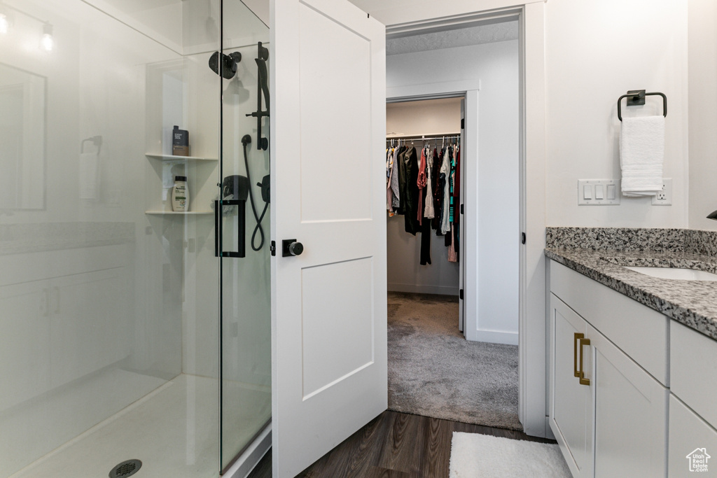 Full bath with a shower stall, vanity, a spacious closet, and wood finished floors