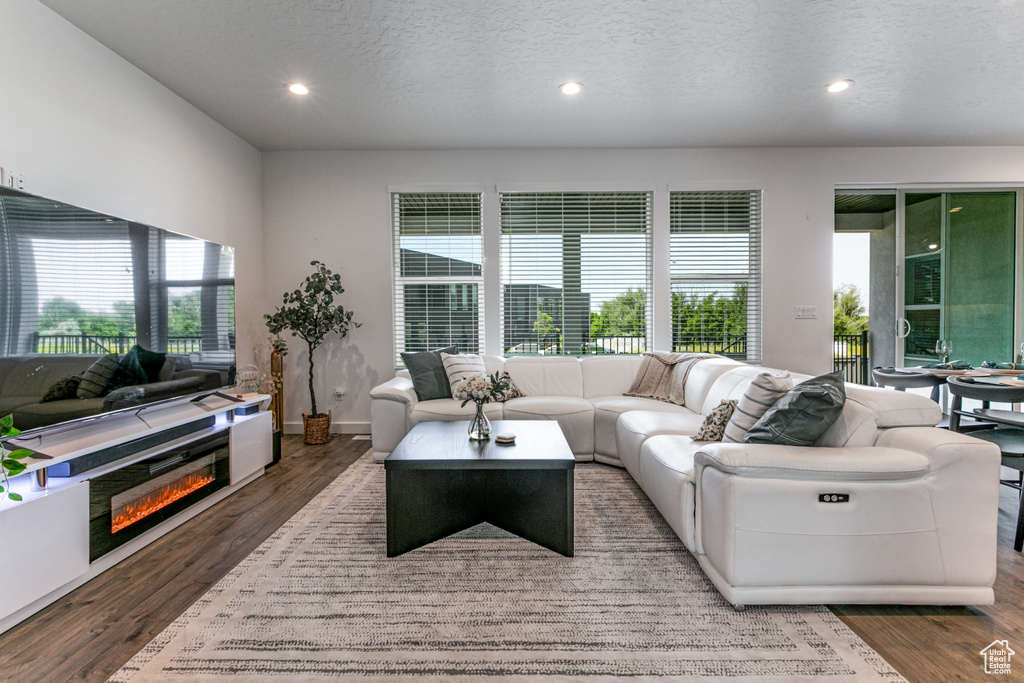 Living area with a textured ceiling, wood finished floors, recessed lighting, baseboards, and a glass covered fireplace