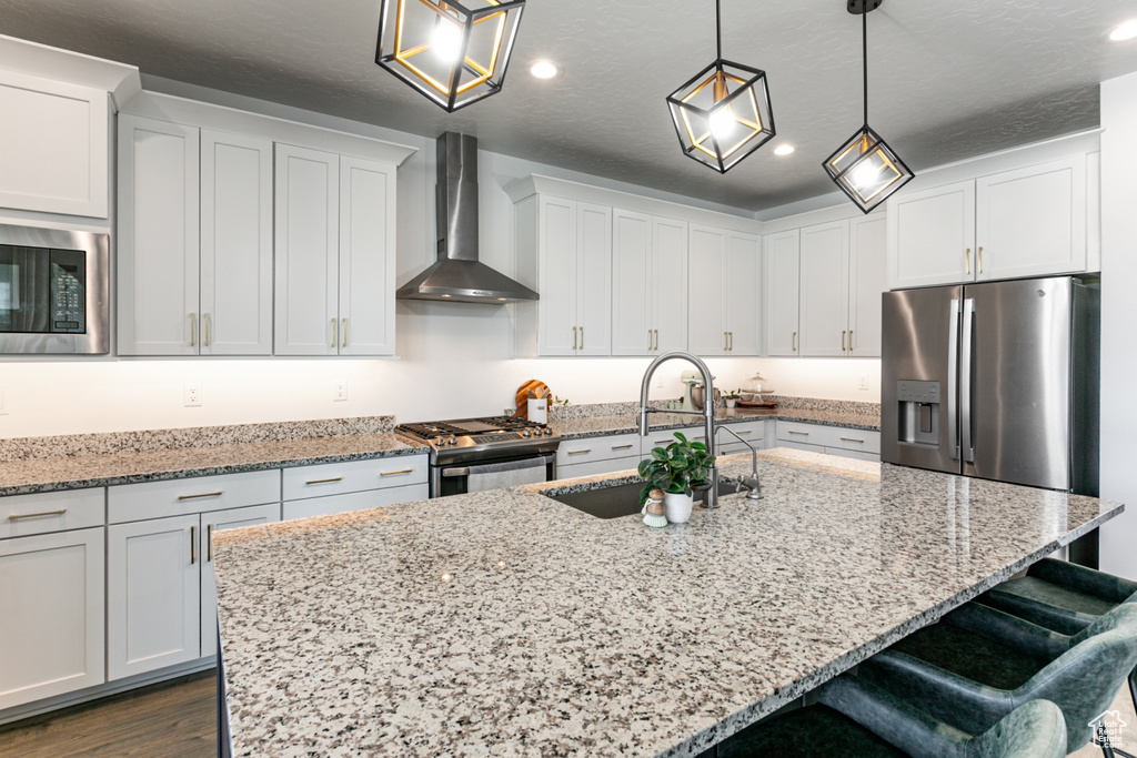 Kitchen with wall chimney range hood, stainless steel appliances, a sink, recessed lighting, and a kitchen bar