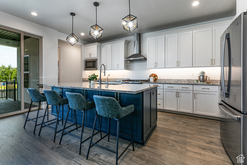 Kitchen with wall chimney exhaust hood, appliances with stainless steel finishes, a sink, dark wood-type flooring, and white cabinets