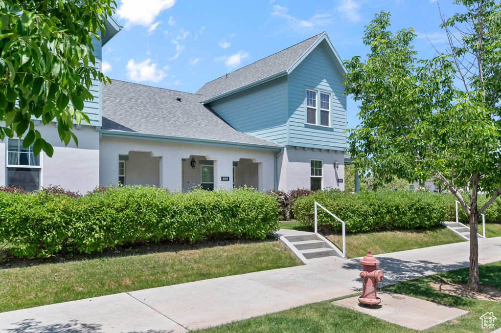 View of front of home featuring a shingled roof, stucco siding, and a front lawn