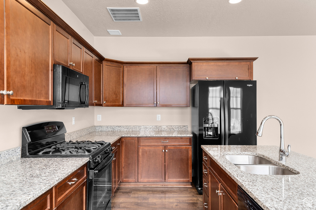 Kitchen with black appliances, a sink, dark wood-style flooring, and light stone counters